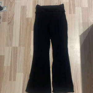 Svarta ribbade yoga byxor från H&M - Svarta byxor från H&M med ribbad, elastisk midja och utsvängda ben. Mjukt material som känns skönt mot huden och ger en avslappnad vibe. Perfekta för dig som gillar bekväma och stilrena plagg med lite extra edge.