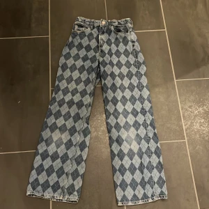 Blå rutiga wide jeans från H&M - Säljer ett par blå jeans från H&M med rutigt mönster i olika nyanser av blått. Modellen är wide med hög midja och justerbar midja. Klassisk femficksdesign och raka ben. Matchar väldigt bra med tajta tröjor.😁