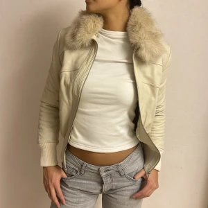 Beige läderjacka med päls  - Snygg beige skinnjacka från Tessie med fluffig päls på kragen och glansigt satin-foder. Min mammas gamla jacka som knappt är använd, har någon brist på armen som syns på sista bilden och lite smuts som knappt märks går säkert att tvätta av. Jackan har dragkedja framtill och en croppad passform som ger en cool vibe. Perfekt för dig som vill sticka ut med en unik look.💋⭐️