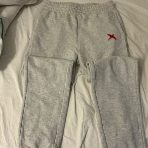 Grå mjukisbyxor från Axel Arigato storlek M  - Grå mjukisbyxor från Axel Arigato med elastisk midja och snörning. Byxorna har en röd broderad fågel på vänster sida och är tillverkade i mjukt bomullsmaterial. Perfekta för chill dagar och har en relaxed passform.