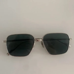 Glasögon från Chimi - Stilrena solglasögon från Chimi med fyrkantiga svarta glas och tunna silvriga metallbågar. Snygg minimalistisk design som ger en modern vibe. Perfekta för dig som vill ha en clean look med edge.