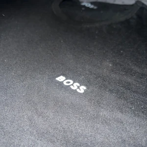 Svart BOSS t-shirt med logga - Svart t-shirt från BOSS med vit logga tryckt på bröstet. Klassisk rund halsringning och korta ärmar. Tillverkad i mjuk bomull för en skön känsla och enkel stil.