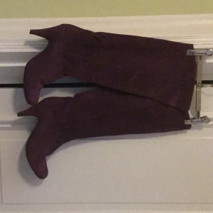 Lila mockastövlar med klack - Säljer ett par höga stövlar i lila mocka med smal klack och spetsig tå. Stövlarna har en elegant och stilren design som sticker ut, perfekta för dig som vill ha något extra. Materialet är mjuk mocka och färgen är djupt lila.