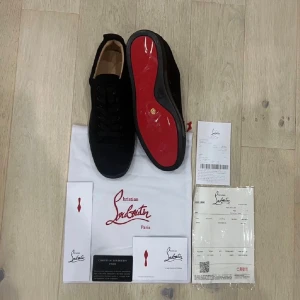 Christian Louboutin svarta sneakers - ❗️Pris kan diskuteras ❗️Snygga svarta sneakers från Christian Louboutin med klassisk röd sula. Skorna har rund tå, snörning och är tillverkade i skinn och textil. Perfekta för dig som vill ha en lyxig och stilren look med en ikonisk touch.