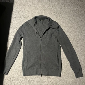 Grå kofta från Massimo Dutti - Snygg grå kofta från Massimo Dutti i extra fin bomull. Modellen har hel dragkedja framtill, ribbade muddar och två fickor. Perfekt för lager-på-lager och chill stil. Passar dig som gillar klassisk look med modern touch.