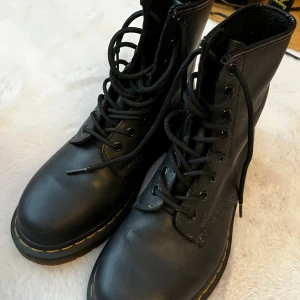Dr. Martens 1460 - Klassiska Dr. Martens 1460 boots i svart skinn med snörning och den ikoniska gula sömmen runt sulan. Grov, genomskinlig sula med bra grepp och rund tå. Perfekta för dig som vill ha en tidlös och edgy stil. Jättefint skick knappt använda. Orginalkartong. 