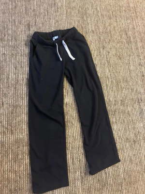Svarta mjukisbyxor med snörning, strl S - Svarta mjukisbyxor från Russedress i storlek S. Byxorna har vit snörning i midjan och är tillverkade i mjukt bomullsmaterial med fleece på insidan. De har en relaxed passform och raka ben, perfekta för chill dagar.