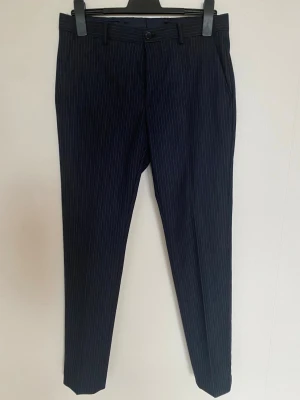 Mörkblå randiga kostymbyxor - Snygga mörkblå kostymbyxor med tunna vita ränder från Riley .Perfekt för en clean och stilren look. 