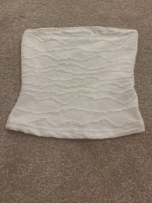 Vit bandeau tubtopp med struktur - Säljer en vit bandeau tubtopp med vågigt strukturerat mönster. Toppen är axelbandslös och har en lätt stretchig passform som sitter snyggt mot kroppen. Perfekt för sommarens varma dagar eller när du vill ha en enkel men cool look.