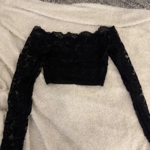 Svart spetsig croppad topp från NLY  - Säljer en svart croppad topp från NLY One i spets med långa ärmar och vacker scallop-kant upptill. Perfekt för dig som gillar detaljer och vill ha en elegant look med genombrutet mönster. Den har även som ett linne under som täcker så den inte är genomskinlig 