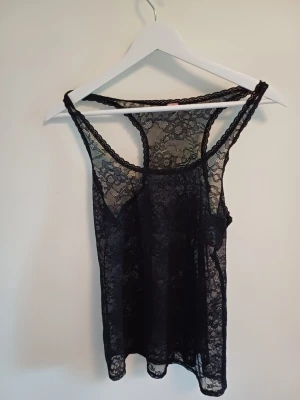 Svart spetsig linnetopp - Säljer en hjäte fin svart linnetopp i genomskinlig spets med blommigt mönster. Toppen är ärmlös och har smala axelband samt rundad halsringning. Skriv för fler frågor ❤️ s/m
