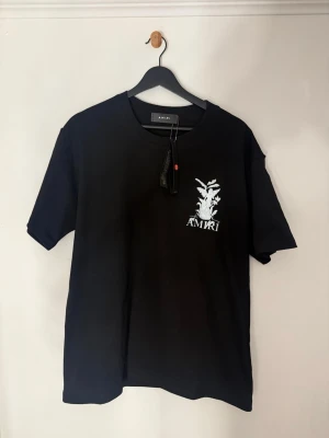 Svart t-shirt med tryck från Amiri - Hej säljer nu denna Amiri t shirt som jag fick i julklapp. Tröjan är size M men jag skulle säga att den passar bättre på någon som har size L. Den är i oversized modell. Riktigt snygg med diskret tryck på framsidan och en större grafisk ängel på ryggen.  Priset är inte hugget i sten!