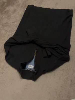 Svart stickad half zip tröja Lindebergh - Svart stickad tröja från Lindebergh med half zip och ribbad struktur. Tröjan har lång ärm och en klassisk krage med dragkedja. Perfekt för kyliga dagar och enkel att matcha med jeans eller chinos.