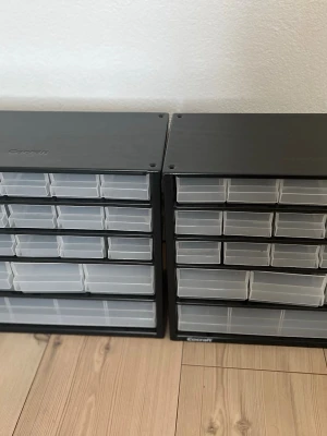 Förvaringslådor med plastfack - 2 st - Bilderna visar två svarta förvaringslådor med genomskinliga plastlådor. Perfekt till små saker så som skruvar, smycken eller annat. Jag säljer båda förvaringslådorna för 450kr, skriv gärna prisförslag.