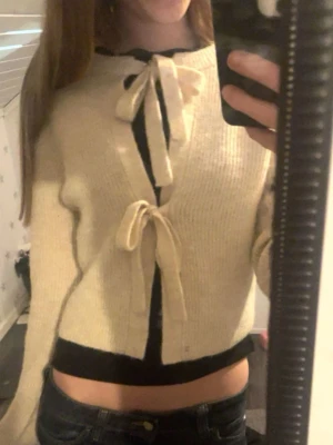 Beige stickad kofta med knyt - Säljer en beige stickad kofta med två snygga knyt framtill. Koftan har en croppad passform och långa ärmar. Perfekt att slänga över en topp för en chill och trendig look. Materialet är mjukt och ribbat, vilket gör den extra skön att bära. Skriv vid förslag av pris!❤️