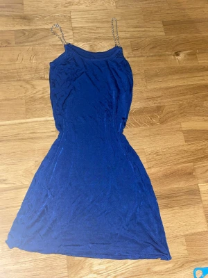 Blå kortklänning med kedjeaxelband - Snygg blå kortklänning med smal passform och kedjeaxelband i silverfärg. Ingen strl står men skulle kunna passa flera strl från Xs till M eller kanske L. Perfekt nu till nyår🥂