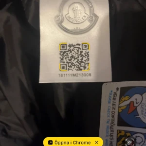 Svart Moncler cardigan  - Svart pufferjacka från Moncler med huva och ribbade stickade ärmar. Jackan har dragkedja framtill och Moncler-logga på ärmen. Materialmix av polyester och stickad textil ger en schysst kontrast. Perfekt för dig som gillar stilren och sportig look.