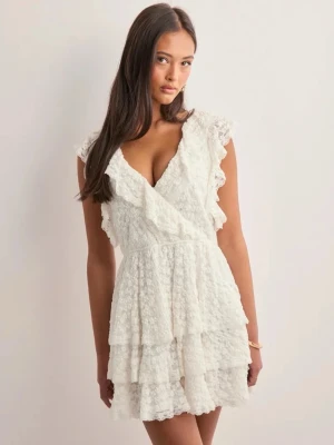 Studentklänning  - Superfin vit kortklänning i spets med omlott och v-ringning. Klänningen har volangdetaljer, är ärmlös och har en öppen rygg med knytband.            Passar perfekt till sommmaren och studenten🩷