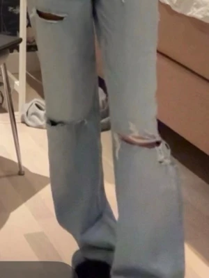 Ljusa jeans ifrån Zara - Säljer ett par ljusblå jeans med breda ben och slitna detaljer över knäna och låren. Jeansen har klassisk femficksdesign och är tillverkade i jeansmaterial. Perfekt för dig som gillar en avslappnad och trendig look. Jättefina jeans ifrån Zara storlek 34 som är slutsålda på hemsidan!! Hållen är lite ut töjda men inte alls mycket❣️