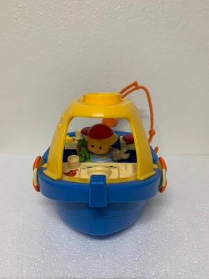 Blå och gul leksaksbåt med figur - Rolig leksaksbåt i plast med blå och gul färg, detaljer i orange och beige. Båten har en liten figur med röd keps och fiskespö, samt flera små tillbehör som fisk och verktyg. Perfekt för fantasifulla lekar och äventyr på land eller i vatten.