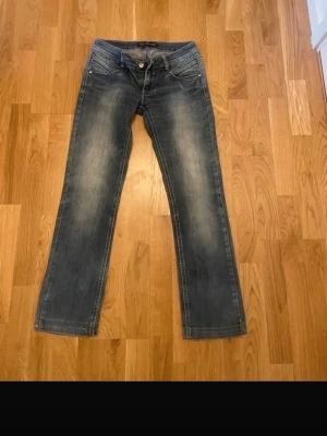 Blå jeans med bootcut - Säljer ett par blå jeans med snyggt slitna detaljer och klassisk bootcut-passform. Jeansen har fem fickor, dragkedja och knapp framtill. Materialet är jeans och färgen är mörkblå med ljusare partier. Perfekt för dig som gillar en avslappnad stil.