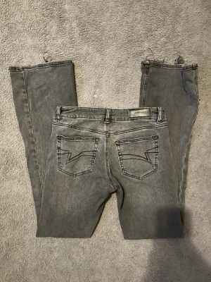 Svart/grå bootcut jeans från Junkyard - Säljer ett par svart/grå bootcut jeans från Junkyard i storlek S. Jeansen har klassisk femficksdesign, råa och slitna benslut samt coola bakfickor med zigzag-söm. Jag har vanligtvis storlek 36 i jeans men tycker att dessa är för stora på mig. Pris kan diskuteras💕