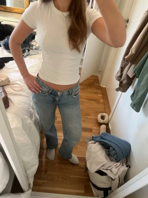 Lågmidjade ljusblå jeans - Säljer ett par riktigt snygga lågmidjade jeans i ljusblå tvätt. Modellen har klassisk femficksdesign och raka ben med lite loose passform. Perfekta för dig som gillar retrovibbar och vill ha en chill look. Materialet är jeans och de har knapp- och dragkedjestängning framtill.
