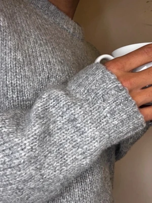 Grå stickad tröja med loose fit - Mysig grå stickad tröja med rund hals och långärmade ärmar. Tröjan har en loose passform och är tillverkad i ett tjockt, stickat material som passar perfekt för kyliga dagar. Enkel och stilren design som är lätt att matcha med olika outfits.