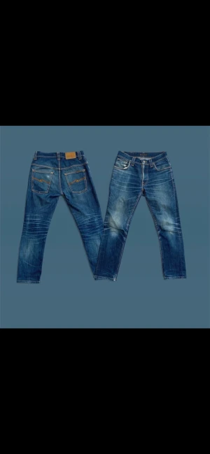Blå jeans från Nudie Jeans Co, storlek 29/32 - Säljer ett par snygga blå jeans från Nudie Jeans Co i storlek 29/32. Jeansen har klassisk femficksdesign, orangea sömmar och slitningar på framsidan för en cool look. Passformen är slim och materialet är robust denim i bomull. 