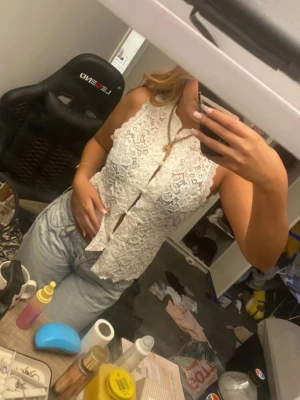 Vit spetsblus med knappar - Säljer en superfin vit blus i spets med knappar framtill och hög krage. Blusen är ärmlös och har en lätt figurnära passform. Perfekt att styla med jeans eller kjol för en trendig look.