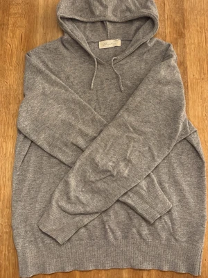 Grå cashmere hoodie från sayless - En ljusgrå cashmere hoodie med huva i storlek small från varumärket sayless. Tillverkad i mjuk cashmere ull med ribbade muddar vid ärmslut och nederkant.