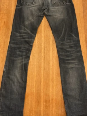 Mörkblå nudie jeans i modellen tube tom  med slitningar i storlek 30/32 - Säljer ett par mörkblå nudie jeans i modellen tube tom med snygga slitningar på både fram- och baksida. Jeansen har klassiska fem fickor och kontrastsömmar. Materialet är denim och har en tvättad look. Jeansen sitter ganska så smått i midjan