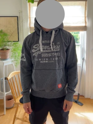 Mörkgrå Superdry hoodie, Storlek L - Superdry Hoodie säljes pga storlek! Bra skick utöver lätt slitage mot trycket.. står som 2XL men skulle säga L!!