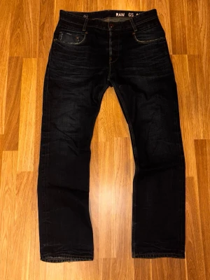 Mörkblå jeans från G-Star RAW - W33 L32 Snygga mörkblå jeans från G-Star RAW med klassisk femficksdesign. Jeansen har kontrastsömmar och en läderpatch bak i midjan. Tillverkade i slitstarkt denim som ger en cool och tidlös look.