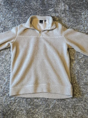 Beige teddytröja från Only & Sons - Mysig beige teddytröja från Only & Sons med halv dragkedja och hög krage. Tröjan är tillverkad i ett fluffigt, stickat material som ger en avslappnad och trendig look. Perfekt för lager på lager och chill dagar.