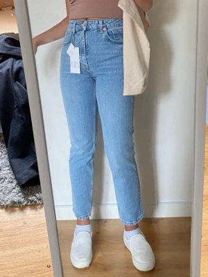 Ljusblå raka croppade jeans med hög midja - Säljer ett par ljusblå jeans med rak passform och hög midja. Klassisk femficksmodell med knappgylf och bälteshällor. Är i ankellängd. (Lappen är inte kvar längre)