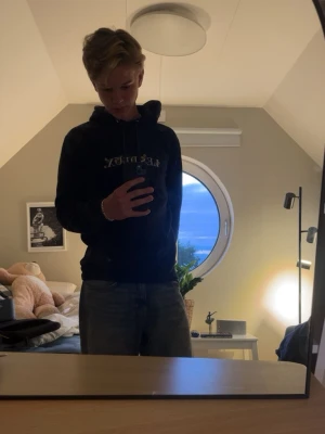 Mörkblå hoodie från Les Deux - Säljer en mörkblå hoodie från Les Deux med broderad text och blommor på bröstet. Hoodien har huva med dragsko och en avslappnad passform. Perfekt för dig som vill ha en stilren men ändå unik look.