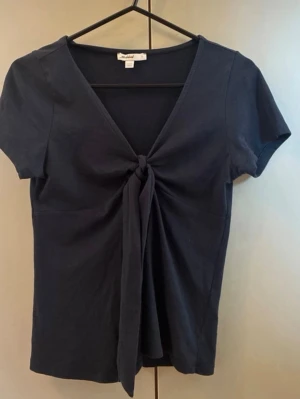 Mörkblå topp med knyt framtill - Snygg mörkblå topp med v-ringning och knyt framtill. Kortärmad modell i mjukt bomullsmaterial som ger en skön känsla. Perfekt till jeans eller kjol. Köpte från subdued men har inte andvänt så mycket 