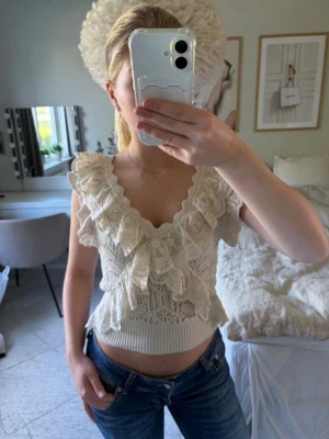 Beige virkad topp med volang - Säljer en supersöt beige virkad topp från Zara i storlek S. Toppen har en fin volang runt v-ringningen och axlarna🧸. Den är ärmlös och har en croppad passform med ribbad midja. Perfekt till både vardag och fest!✨