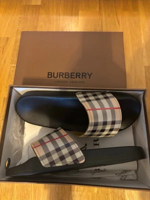 Burberry Tofflor - Oanvände Burberry tofflor. Storlek 46 men funkar även som 45. Påse ingår även i paketet. De har jag lagt upp till salu då jag inte riktigt behöver de.