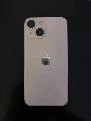 Ljusrosa iPhone 13 mini - Säljer en ljusrosa iPhone med stilren design och rundade hörn. Baksidan har två stora kameralinser och Apples logga i silver. Framsidan har en stor skärm med Face ID och tunna kanter. Materialet är glas och metall, vilket ger en premiumkänsla.