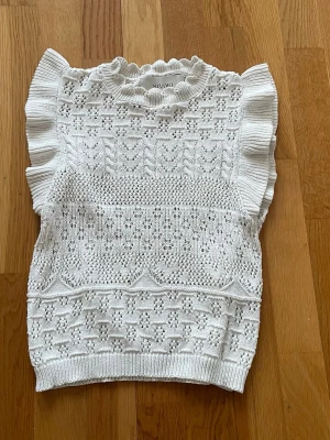 Vit virkad topp från ONLY  - Supersöt vit virkad topp från ONLY med volangdetaljer vid ärmarna och ett fint hålmönster över hela plagget. Rundad halsringning med liten volangkant. Perfekt för dig som gillar romantisk och trendig stil.