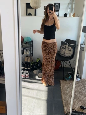 Lång genomskinlig kjol med leopardmönster - Säljer en snygg lång genomskinlig kjol med leopardmönster i bruna och svarta toner. Kjolen har en rak passform och är tillverkad i ett mjukt, lätt material som faller fint längs benen. Perfekt för dig som vill sticka ut med en trendig look. Använd en gång