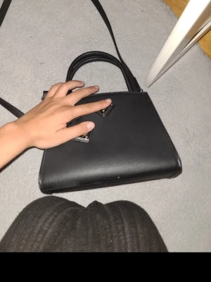 Handväska  - Snygg svart handväska i skinnimitation med både handtag och axelrem. Väskan har silverfärgade metalldetaljer och en enkel, stilren design som passar till många olika outfits. Perfekt för dig som gillar minimalistisk och modern stil.  Pris går att diskutera vid snabb affär, skriv för mer bilder 