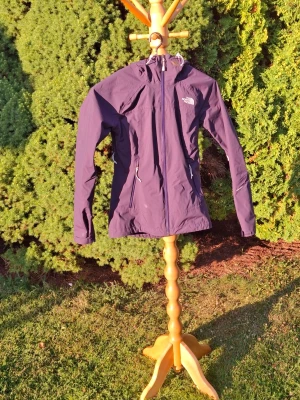  regnjacka från The North Face - Snygg lila regnjacka från The North Face med huva och dragkedja framtill. Jackan har två fickor med dragkedja och justerbar nederkant. Insidan har meshfoder för extra ventilation. Perfekt för regniga dagar och outdoor-äventyr. Kontakta gärna mig vid funderingar!