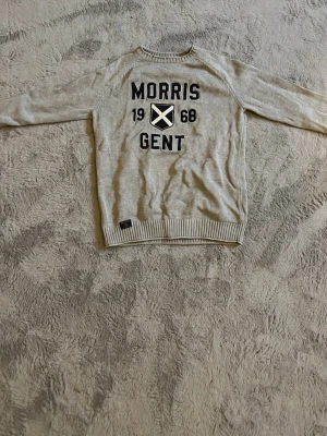 Grå tröja med tryck från Morris - Snygg grå tröja från Morris med svart tryck 'Morris Gent 1968' och ett vitt kors på bröstet. Tröjan har rund hals, långa ärmar och ribbade muddar vid ärmslut och nederkant. Perfekt för en avslappnad och stilren look. Har dock ett litet hål under armen men kan enkelt lagas.