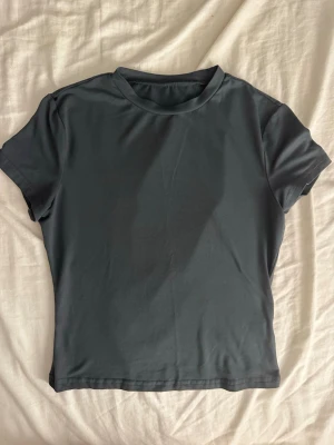 Mörkgrå basic t-shirt - En enkel och stilren mörkgrå t-shirt med rund hals och korta ärmar. T-shirten har en normal passform och är tillverkad i mjukt material, perfekt för en clean och avslappnad look.