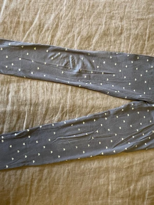 Mörkgråa leggings med silvriga hjärtan - Supersöta mörkgrå leggings med små vita hjärtan över hela tyget. Stl.122/128 från Cubus 
