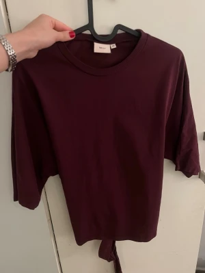 Vinröd topp med knyt från Nelly - Säljer en vinröd topp från Nelly med korta ärmar och snygg knytning i ryggen💞