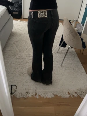 Svarta bootcut jeans med patch - Säljer ett par svarta bootcut jeans i denim med en unik patch på bakfickan. Jeansen har låg midja och klassisk femficksdesign. Materialet är stretchigt för extra komfort och passform. Perfekta för dig som gillar en trendig och avslappnad look.